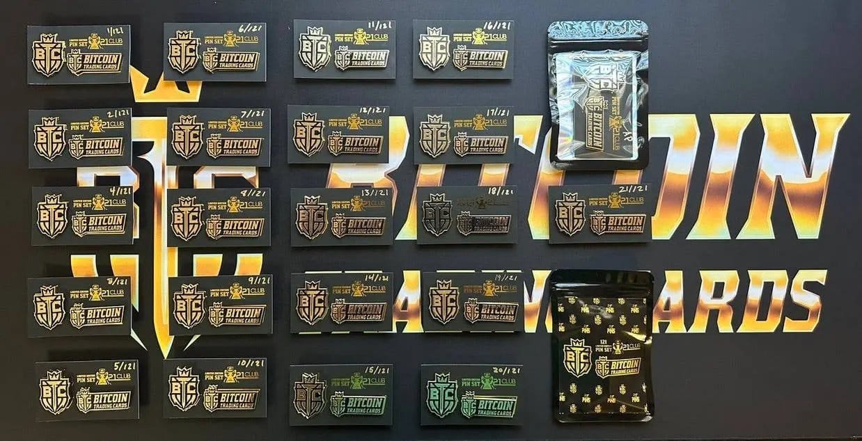 Photograph of a collection of 21 '21 Club' Limited Edition Pin Sets laid out in a grid pattern on a branded mat, showing handwritten serial numbers from '1/121' to '21/121', accompanied by two packaged sets.