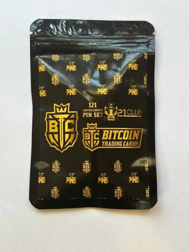Photograph of the back of the '21 Club' pin set packaging, featuring a black background with a repeating gold foil pattern of 'BTC PINS' and shield logos, with text reading '121 LIMITED EDITION PIN SET' and the Honey Badger logo.