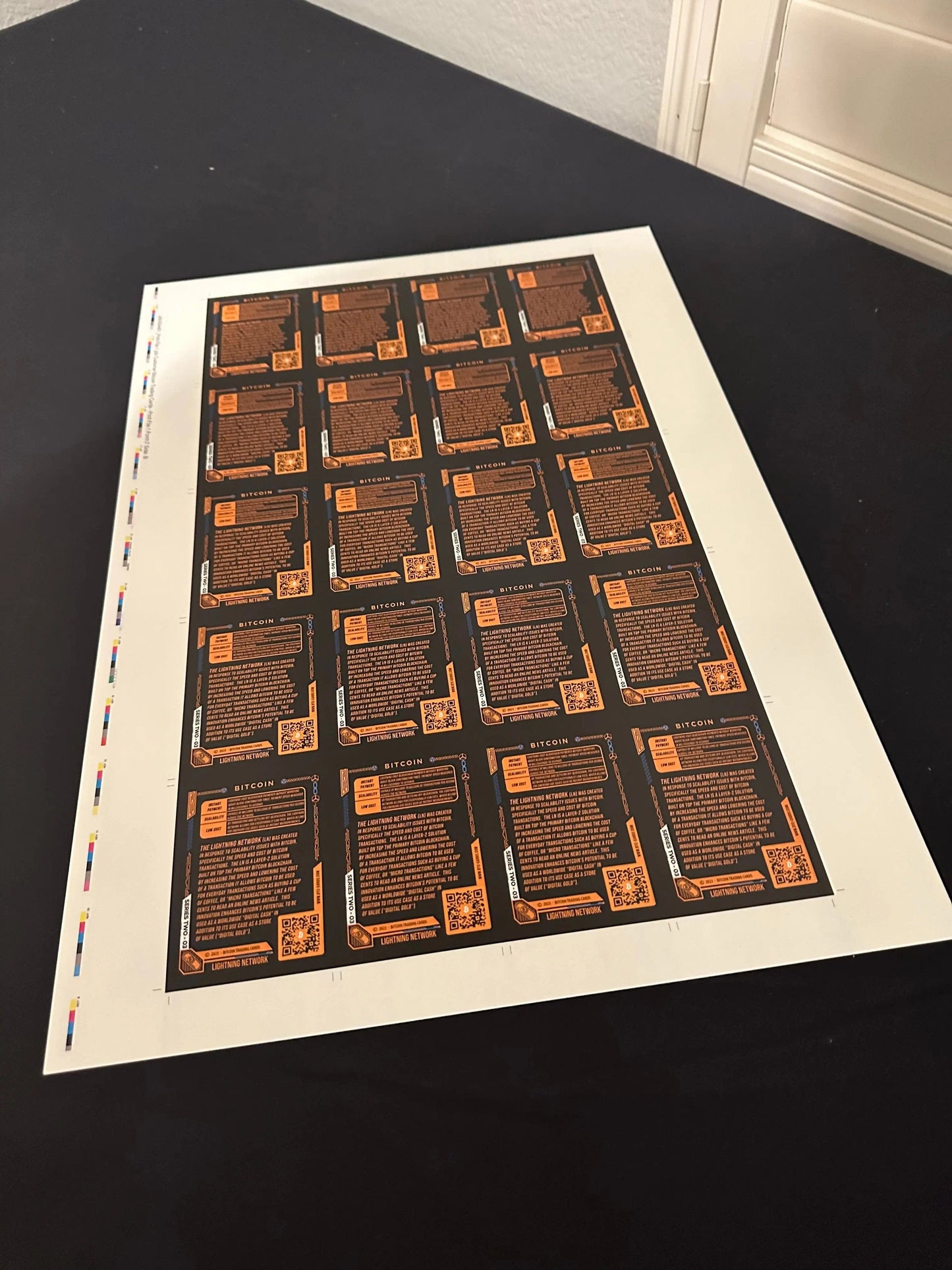 Alternate angle photograph of an uncut production press sheet for Bitcoin Trading Cards lying on a table, showing the educational text on the back of the 'Lightning Network' cards. 
