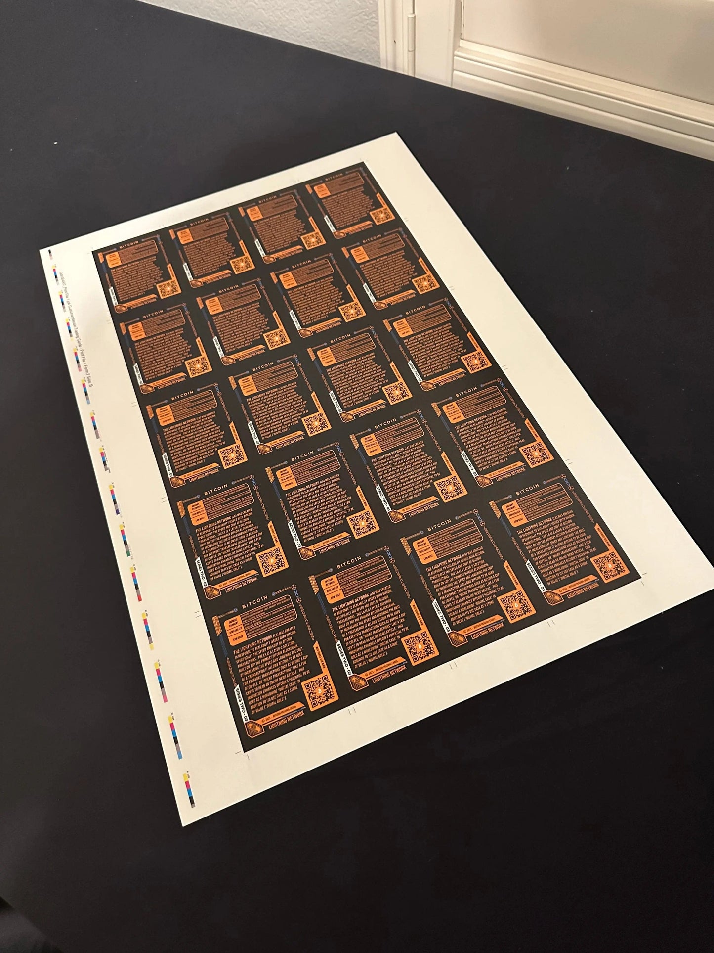 High-angle photo of a full uncut production press sheet for Bitcoin Trading Cards lying on a black table, displaying the text side of the 'Lightning Network' cards with production color bars.