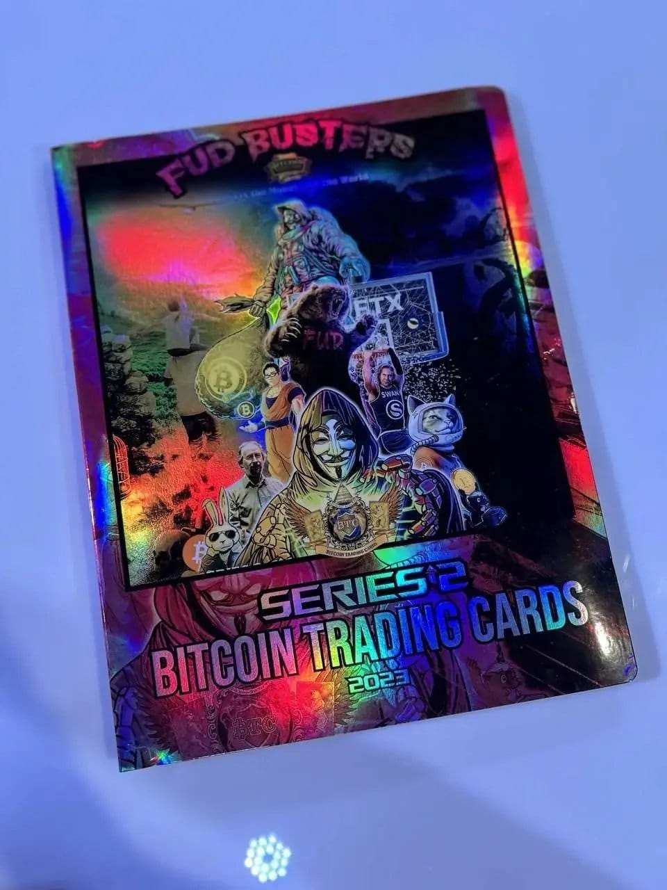 Photograph of the physical Bitcoin Trading Cards Series 2 'FUD Busters' cover art, displaying a reflective rainbow holographic foil finish.