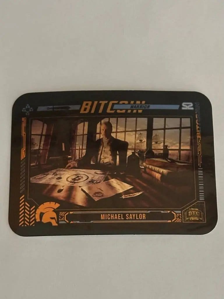 Close-up photograph of the limited edition 'Michael Saylor' sticker from the Series 2 collection, depicting him as a 'Bitcoin Warrior' sitting at a wooden desk with a map, quill, and nautical instruments.
